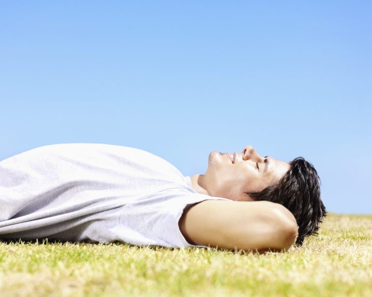 Junger Mann liegt entspannt auf dem Gras und schaut in den blauen Himmel.